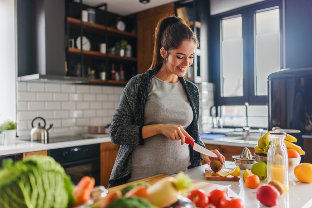 Pregnant woman preparing healthy food with lots of fruit and vegetables at home kitchen