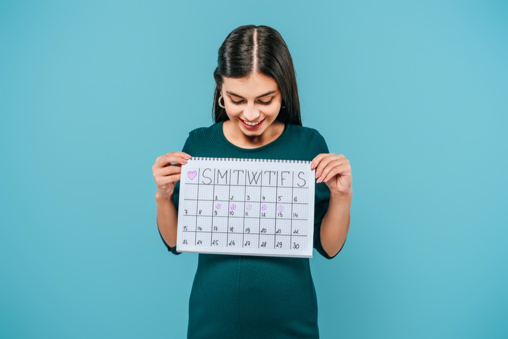 smiling pregnant girl looking at period calendar